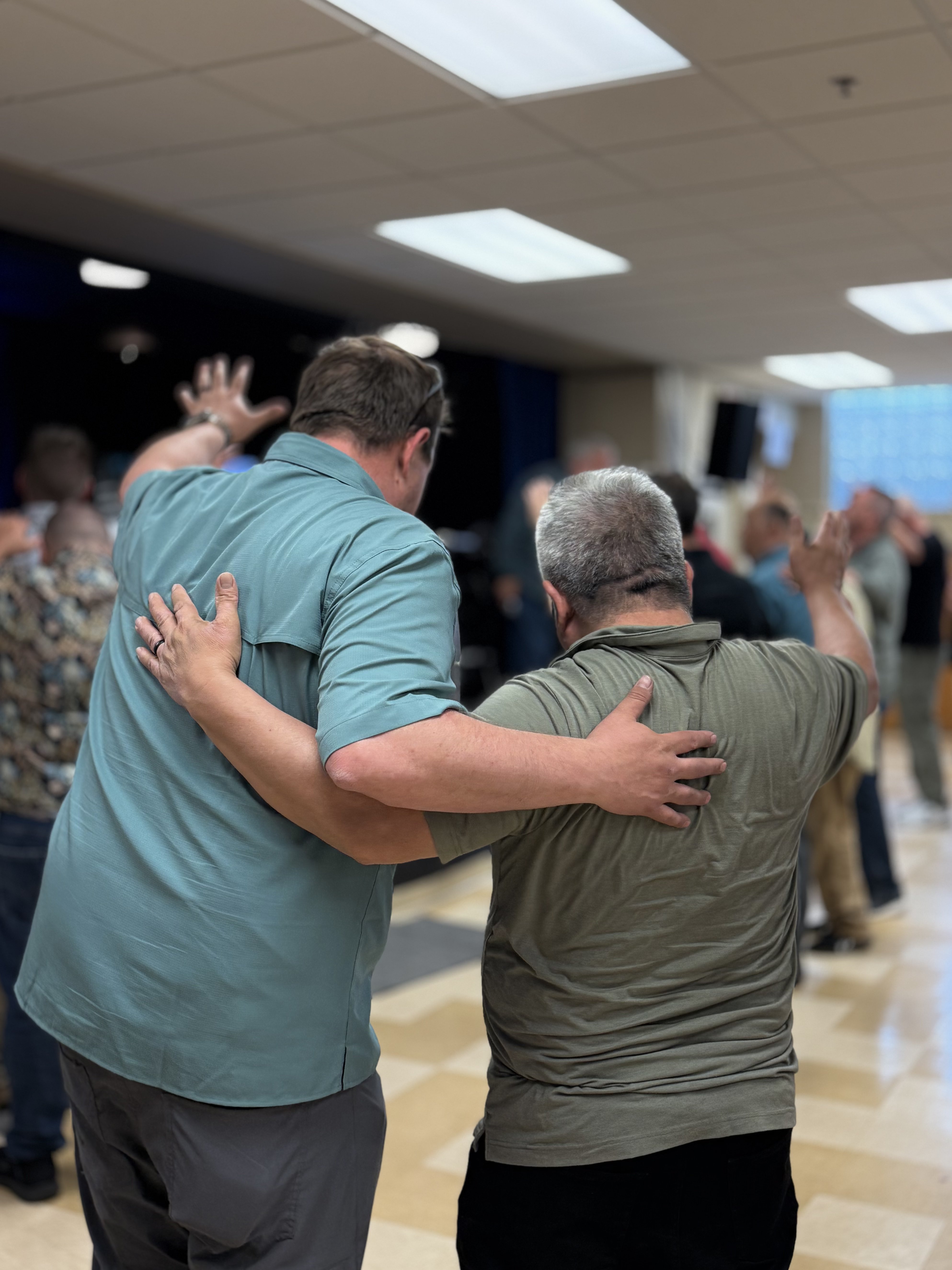Men with hands raised in brotherhood worship at Wisconsin Iron Sharpens Iron event